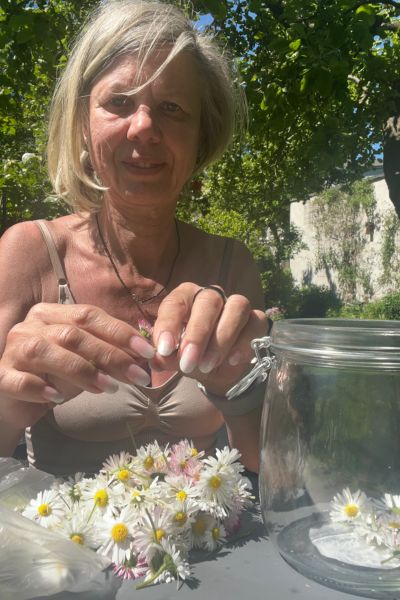 Monatsrückblick Mai 2026: blonde Frau sitzt am Tisch und bereitet Gänseblümchenblüten für eine Tinktur vor