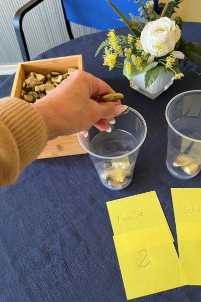 Kind lernt trotz Üben nicht: Goldnuggets stehen auf dem Tisch, Becher werden mit Goldnuggets gefüllt, jeder Becher steht für einen Bereich wie Schule, Hausaufgaben, Familie, Hobby