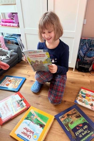 Fun Facts Legasthenie und ADHS: blondes Mädchen sitzt umgeben von mehreren Büchern und liest freudvoll