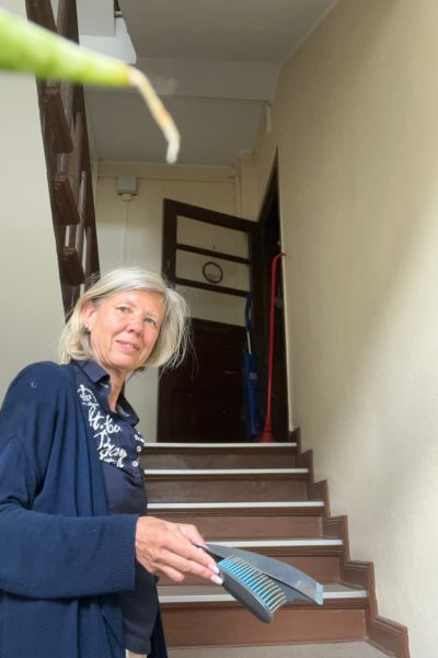 12 von 12 im August 2026: Frau Mitte fünfzig steht im Treppenhaus und hält Handfeger und Schaufel in der Hand