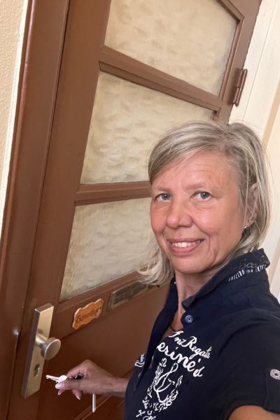 12 von 12 im August 2026: Frau Mitte fünfzig steht vor einer Wohnungstür und steckt den Schlüssel ins Schlüsselloch