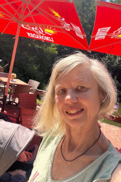 Bucket List fürs Leben: Porträt einer blonden Frau über 50 sitzend unter einem roten Sonnenschirm