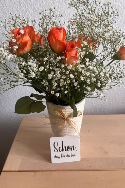 12 von 12 im September 2026: organgefarbene Rosen in heller Vase auf dem Tisch, davor ein Schild mit der Aufschrift: Schön, dass es dich gibt