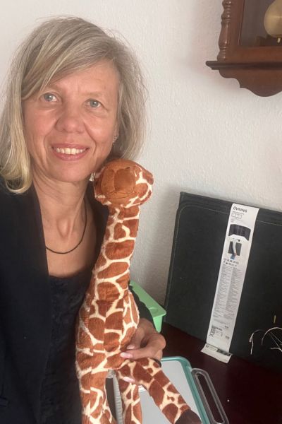 12 von 12 im September 2026: blonde Frau mit mittellangen Haaren in blauem Blazer hält eine Giraffe als Plüschtier in der Hand