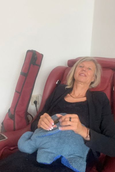 12 von 12 im September 2026: blonde Frau mit mittellangen Haaren in blauem Blazer sitzt im Massagesessel und hält einen blauen genähten Elefanten in der Hand