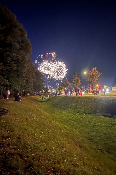 Monatsrückblick August 2026: im Vordergrund ein begrünter Wall, links Bäume und im Hintergrund ein strahlendes Feuerwerk