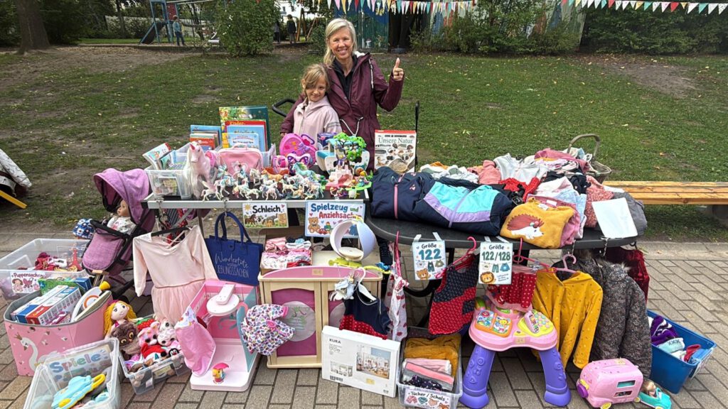Monatsrückblick Oktober 2026: blonde fünfzigjährige Frau und achtjähriges Mädchen hinter einem bunten Flohmarktstand